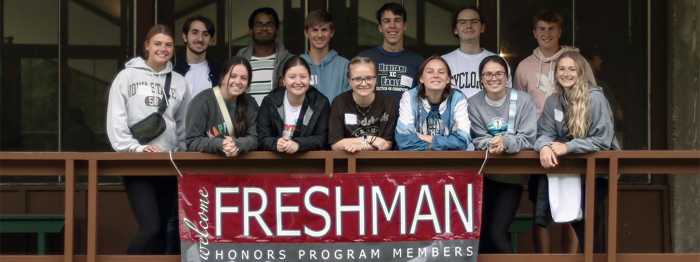 Group of honors students posing for a group photo in front of the "Welcome Freshmen Honors Program Members" banner at the 2023 FHP Retreat.