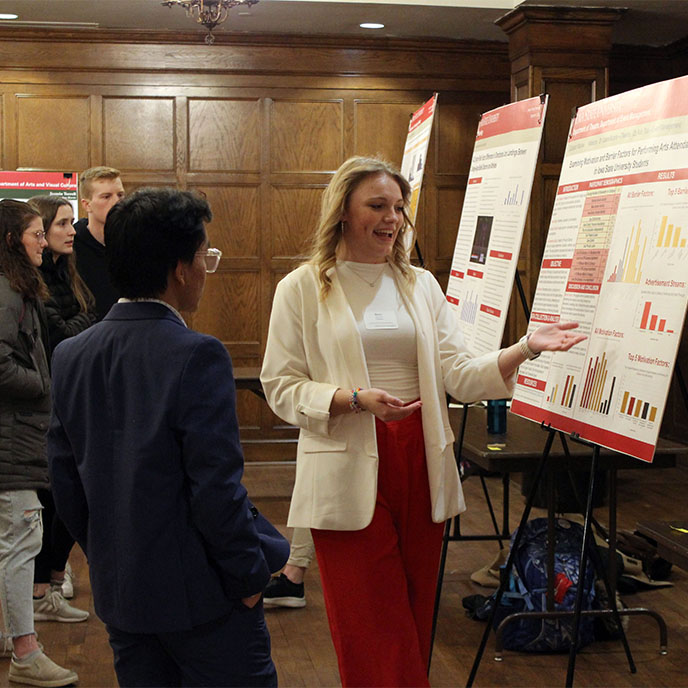 Female honors student presenting her research at the poster session to another honors student.